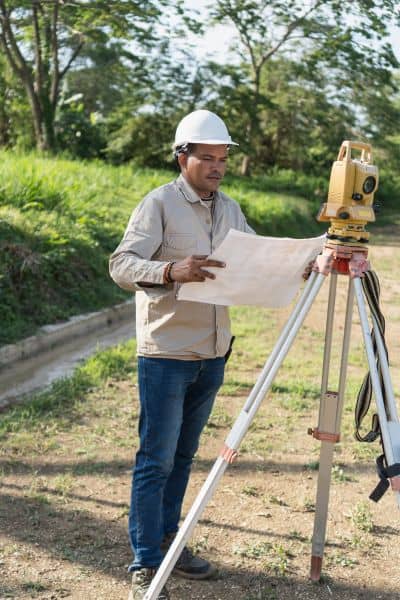 Due diligence survey property verification - ALTA SURVEY New York Land surveyor reviewing site plans beside a total station for a due diligence survey